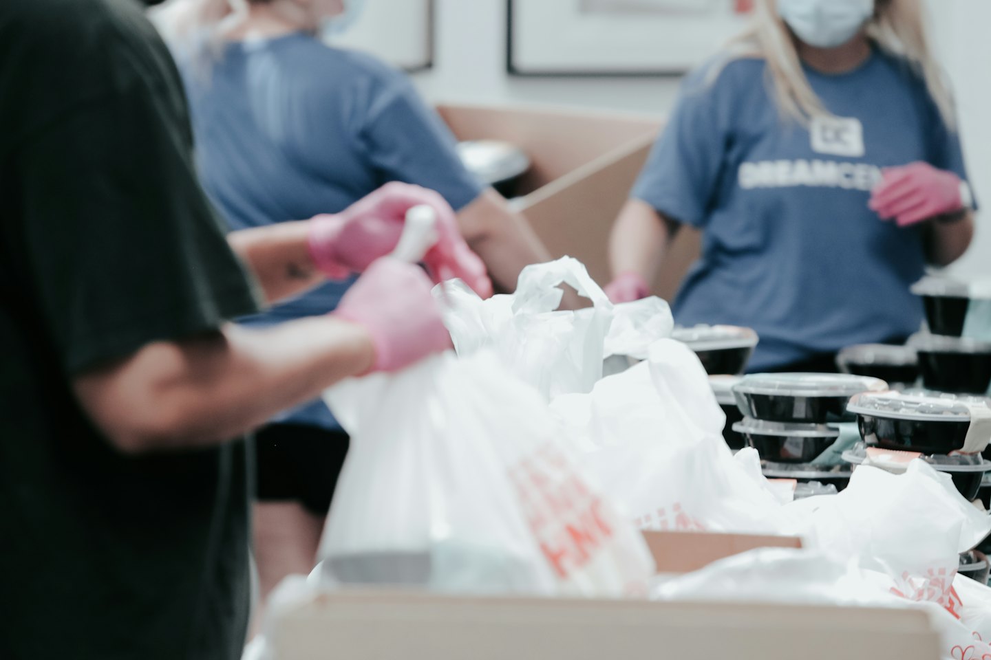 Volunteers in pink gloves fill bags with food for distribution.